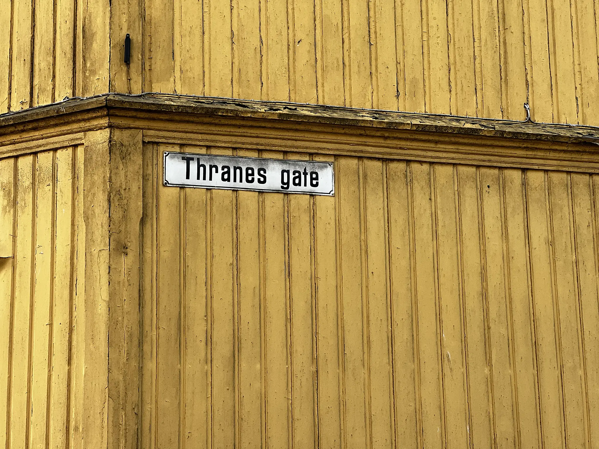 Gammelt gateskilt med teksten Thranes Gate på gul rustikk vegg.
